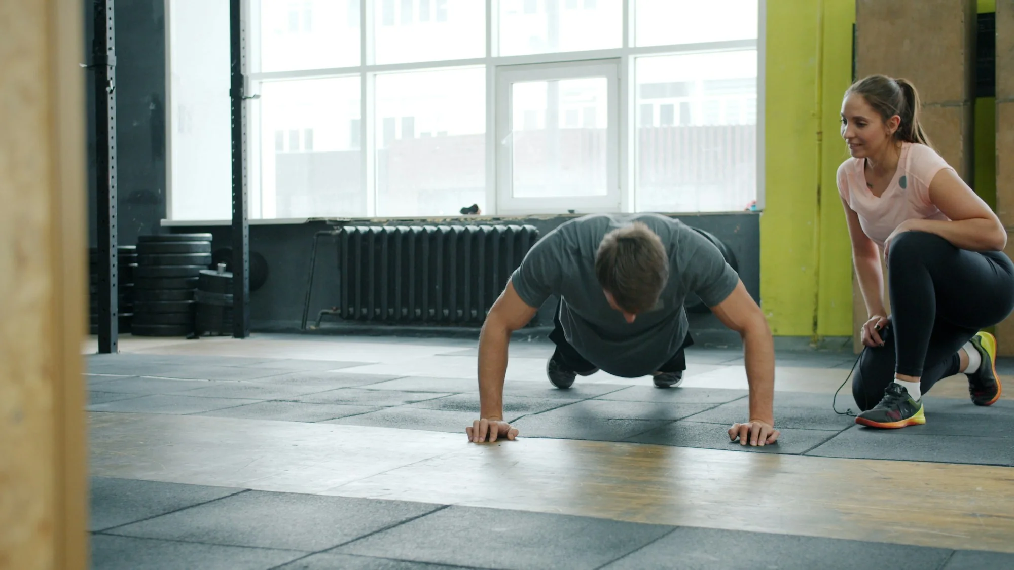 Une coach accompagne une personne qui effectue des pompes dans une salle
